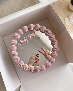 a pink cake in a white box with the words happy birthday written on it and someone's hand making a peace sign