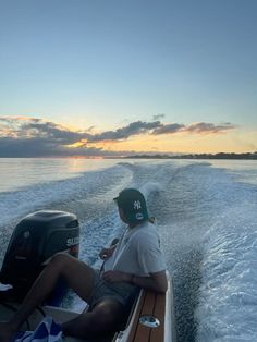 a man sitting on the back of a boat in the middle of the ocean at sunset