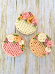 three decorated cookies sitting on top of a white wooden table next to an orange and pink frosted cookie