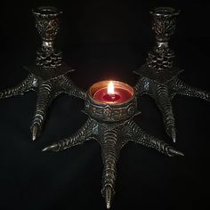 three metal candlesticks sitting next to each other on a black surface with one lit candle in the middle