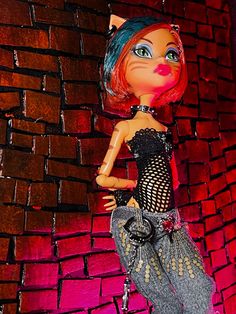 a cat doll is posed in front of a brick wall and holding onto a purse