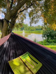 a book is laying in a hammock next to a tree and water on a sunny day