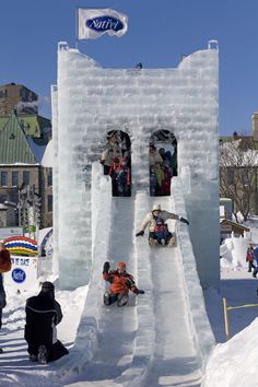 several people are sitting on an ice castle in the middle of town, while others watch