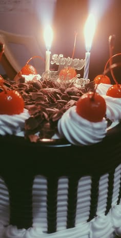 a cake with white frosting and cherries has two lit candles on the top