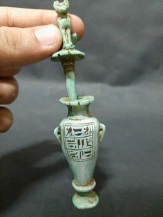 a small green vase with an egyptian decoration on it's side, being held by a hand