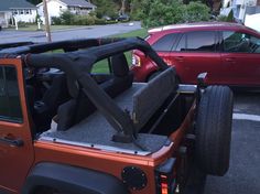 an orange jeep with its doors open in a parking lot next to a red car
