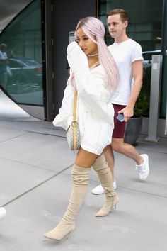 a woman with pink hair walking down the street while wearing thigh high boots and a white shirt