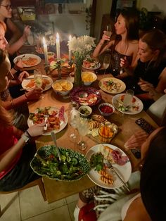 a group of people sitting around a table with plates of food and candles on it