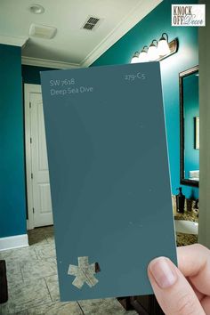 a hand holding up a blue paint swatch in a bathroom that is painted teal