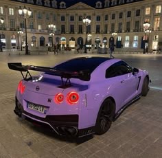 a purple sports car parked in front of a large building at night with its lights on
