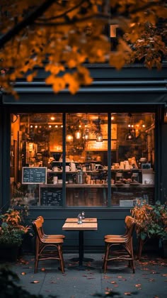two wooden chairs sitting at a table in front of a restaurant window with fall leaves on the ground