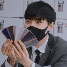 a man holding a fan and wearing a black face mask with his mouth covered in color swatches