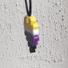 a yellow, white and purple necklace hanging from a black cord on a concrete wall