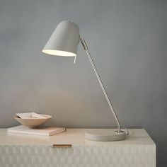 a white lamp sitting on top of a table next to a bowl and book shelf