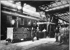 an old black and white photo of men standing in front of train cars at a station