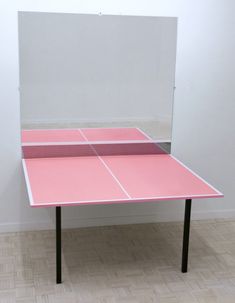 a pink ping pong table sitting on top of a hard wood floor next to a white wall