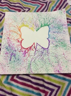 a butterfly made out of paper on top of a colorful blanket with paint splattered all over it