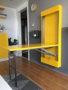 a yellow desk in the middle of a room with a clock on the wall behind it