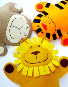 three felt animals are laying next to each other on a white surface, one has a tiger and the other is a lion