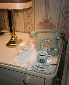 an old fashioned telephone sitting on top of a table next to a cup of coffee