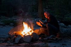 a man sitting in front of a campfire at night with his hands out to the side