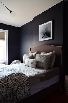 a bedroom with black walls and white bedding in the corner, along with two framed pictures on the wall