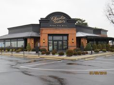 an empty parking lot in front of a restaurant with lots of windows and bushes on each side