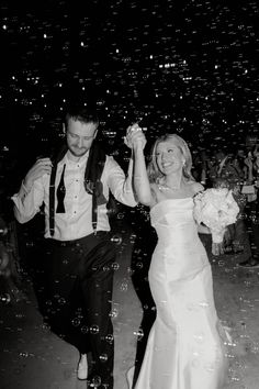 a bride and groom walking through bubbles at their wedding reception in black and white photo