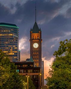 a large clock tower towering over a city at dusk with trees in the foreground