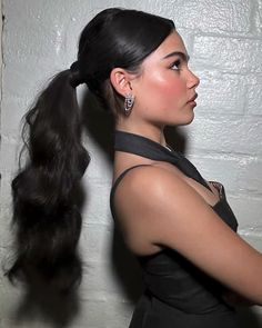 a woman with long black hair standing in front of a white wall