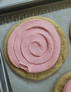 three cookies with pink frosting on a baking sheet