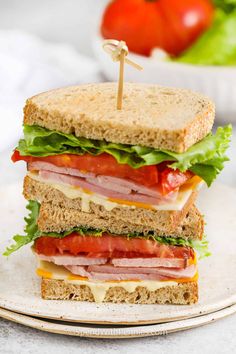 a sandwich with ham, lettuce and tomato on it sitting on a plate