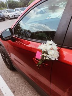 a bouquet of flowers is placed on the side of a red car in a parking lot
