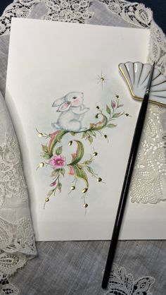 a white card with a rabbit on it next to a fan and lace doily