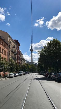 an empty street with cars parked on both sides and a tall tower in the background