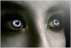 a woman's face with blue eyes and long eyelashes, looking directly into the camera