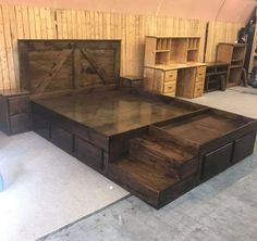 a wooden bed frame with drawers underneath it in a room filled with shelves and other furniture