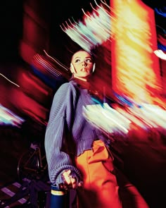 a woman standing next to a bike in front of a building with bright lights on it