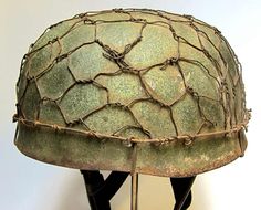 an old green helmet with barbed wire on the top and bottom is sitting on a stand