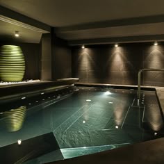 an indoor swimming pool with lights on the wall and water in the middle, surrounded by black tiles