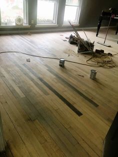 an empty room with wood flooring and paint cans on the floor next to two windows