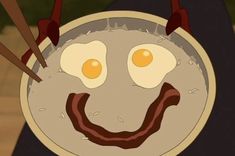 a plate with eggs and bacon on it that looks like a smiley face is being held by two chopsticks