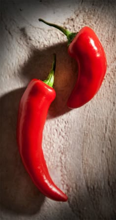 two red peppers sitting next to each other on a white surface with the shadow of a person's head