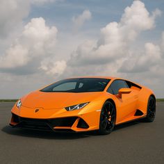 an orange sports car is parked on the pavement with clouds in the sky behind it