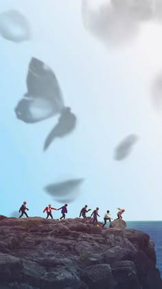 a group of people running on top of a cliff next to the ocean with birds flying overhead