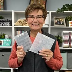 a woman holding two pieces of clear plastic in front of a book shelf filled with books