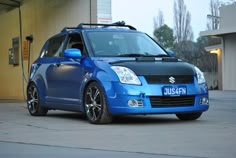 a small blue car parked in front of a building with an electric charger attached to it's roof