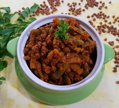 a green bowl filled with chili and beans on top of a table next to some leaves