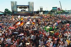 a large group of people standing around each other in front of a stage with flags