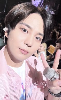 a young man holding a microphone and making the peace sign with his hand in front of him